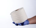 Right hand in blue glove holding with thumb a roll of toilet paper Royalty Free Stock Photo