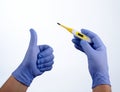 Right hand in blue glove holding a yellow medical thermometer, left hand thumb up