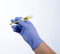 Right hand in blue glove holding a yellow medical thermometer