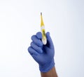 Right hand in blue glove holding a yellow medical thermometer Royalty Free Stock Photo