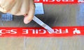 The right hand opening a box with fragile label using a small cutter,