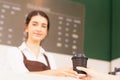 Right side of takeaway coffee cup in two hands of customer and beautiful caucasian barista woman who looks at other place,