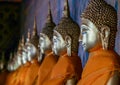 Right side view of a row of golden Buddhas statues seated along the wall wrapped in orange cloth. Royalty Free Stock Photo