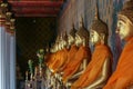 Right side view of a row of golden Buddhas statues seated along the wall wrapped in orange cloth. Royalty Free Stock Photo