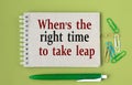 WHEN IS THE RIGHT TIME TO TAKE LEAP - words on a gray notebook with pen and paper clips Royalty Free Stock Photo