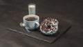right view on an aromatic black coffee in a white cup with coconut liqueur in a glass, with two oreo doughnut on a black stone pl