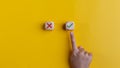 Right and wrong icons on wooden cubes with hand choosing the right icon on yellow background. Approving, voting, or right decision