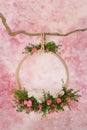 A ring of green twigs and pink roses hangs on a branch, for photos of newborn babies