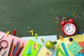 Ringing alarm clock, green apple and school supplies on chalkboard flat lay and top view. Back to school and education concept.