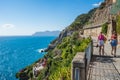 Riomaggiore ITALY - August 2, 2023 - Cliff with vegetation and pathway with two tourists walking in viewpoint towards the sea