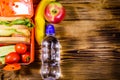 Ripe apple, banana, bottle of water and lunch box with sandwiches, cucumbers and tomatoes on wooden table. Top view Royalty Free Stock Photo