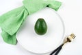 Ripe avocado in a plate next to a green napkin and Cutlery on a light background. Royalty Free Stock Photo