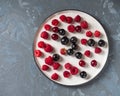 Ripe berries on a light round plate close-up top view