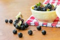 Ripe black chokeberries aronia melanocarpa in a white bowl on red napkin on wooden table.