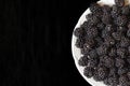 Ripe blackberries in a white plate on a black background close-up. Juicy black berries lie in darkness Royalty Free Stock Photo