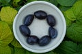 White bowl with ripe plums on green leaves