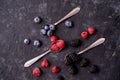 Ripe blueberries, raspberries, blackberries, Mixed berries with three spoons. Various fresh summer berries on dark solid backgroun