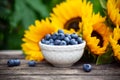 Ripe blueberries in white bowl with sunflower bouquet on wooden table, summer theme Royalty Free Stock Photo