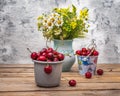 Ripe cherries in a gray mug and a decorative bucket, a bouquet of wild flowers in a blue vase