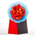 Ripe cherry berries with water droplets into blue plate on black and red strips of paper and resembling an icon Royalty Free Stock Photo