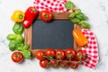 Ripe cherry tomatoes, mini bell peppers, fresh basil leaves on stone table with chalkboard, cooking ingredients top view Royalty Free Stock Photo