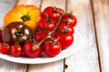 Ripe colorful yellow and red tomatoes on white plate, wooden background. Variety of shapes, colors. Healthy light summer meal, Royalty Free Stock Photo