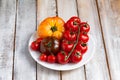 Ripe colorful yellow and red tomatoes on white plate, wooden background. Variety of shapes, colors. Healthy light summer meal, Royalty Free Stock Photo