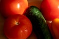 Ripe cucumber, juicy tomatoes and sweet peppers on a light wooden table in the sun. Close up Royalty Free Stock Photo