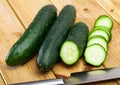 Ripe cucumbers and knife on wooden cutting board