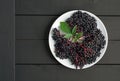 Ripe elderberry in plate on wooden black background