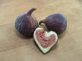 Ripe fig fruits with purple skin and a half of pink figs in the shape of a heart against the background of an old wooden table.