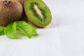 Ripe fleshy green kiwi with juicy slice, young leaves on soft light white table, closeup, top view. Royalty Free Stock Photo