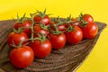 Ripe fresh Juicy organic cherry tomatoes on branch in wooden plate on yellow background Royalty Free Stock Photo