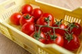 Ripe fresh Juicy organic cherry tomatoes on branch in yellow plastic crate on wooden background