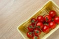 Ripe fresh Juicy organic cherry tomatoes on branch in yellow plastic crate on wooden background