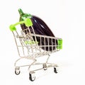 A ripe glossy eggplant lies in a miniature metal cart on wheels on an isolated background Royalty Free Stock Photo