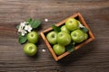 Ripe green apples with branch of white flowers in wooden box on a wooden table