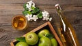 Ripe green apples in wooden box with branch of white flowers, glass and bottle of cider on a wooden table