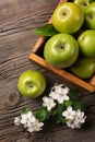 Ripe green apples in wooden box with branch of white flowers on a wooden table