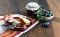 A jar of homemade fruit jam, ripe plums, bread and butter on a red plate. Dark wooden table.