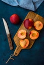 Ripe juicy nectarines, cut in half, whole on wood cutting board, knife, dark blue background, top view, flat lay