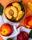 Ripe juicy peaches whole and cut on a wooden plate with green leaves on a white kitchen towel