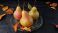 Ripe pears and yellow autumn leaves on a black wooden table in a plate Royalty Free Stock Photo