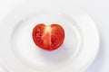 A ripe juicy red tomato cut in half in the form of a heart with drops of water lies on a plate. The view is straight. White Royalty Free Stock Photo