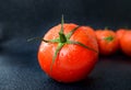 Ripe juicy red tomato with green leaves on a dark background. On tomatoes water drops, clean.