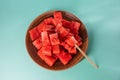 Ripe juicy red watermelon cubes in a brown clay plate on blue background. Watermelon cubes ready for eat