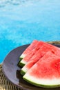 Ripe Juicy Seedless Watermelon Cut in Slices Wedges on Plate on Rattan Table by Swimming Pool. Sunlight. Vacation Relaxation