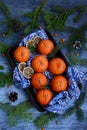 Ripe, juicy tangerines on a blue napkin, orange sea buckthorn berries, fir branches and cones on a blue background