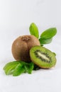 Ripe kiwi with juicy slice and drop juice, green young leaves on white soft wood board, vertical.