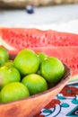 Ripe limes in bowl and watermelon slices. Sweet tropical fruits. Juicy fruits. Fresh limes. Citrus harvest. Colorful fruits. Royalty Free Stock Photo